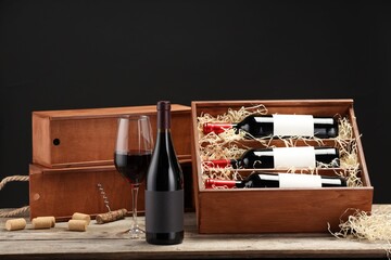 Box with wine bottles, glass, corks and corkscrew on wooden table against black background