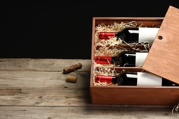 Box with wine bottles on wooden table against black background. Space for text