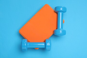 Two dumbbells and yoga block on light blue background, top view