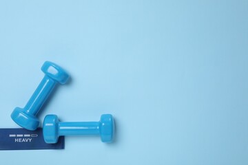 Two dumbbells and fitness elastic band on light blue background, flat lay. Space for text