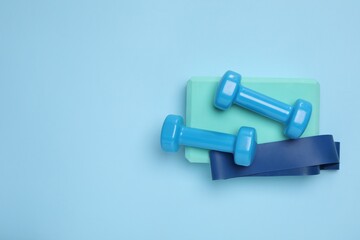 Two dumbbells, yoga block and fitness elastic band on light blue background, top view. Space for text