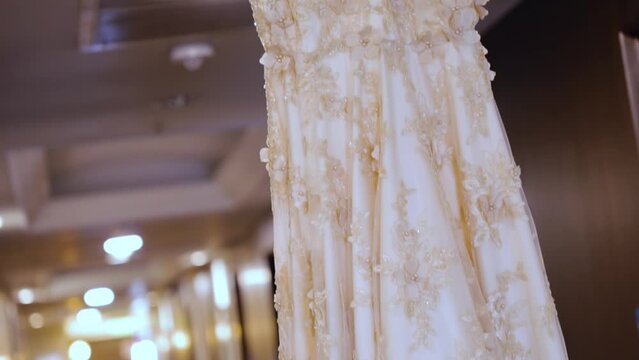 Beige wedding gown hangs on a wooden hanger from the celling 60fps
