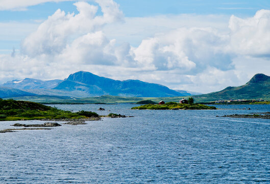 View of Vinstre lake with houses on an island and Jotunheimen mountains in the background