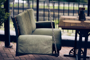 A wooden swing bench is suspended on chains on the summer veranda in the open air. The concept of...