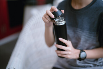 Person holding and opening a thermos or black insulated bottle. There is a metal border around it....