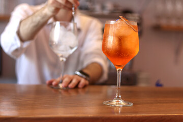 Orange cocktail with a person making another one in the background on the bar counter