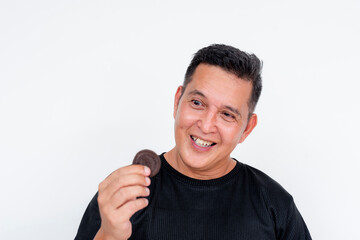 A middle aged Asian man looks at a cookie looking obsessed with eating it. Intense craving or sugar...