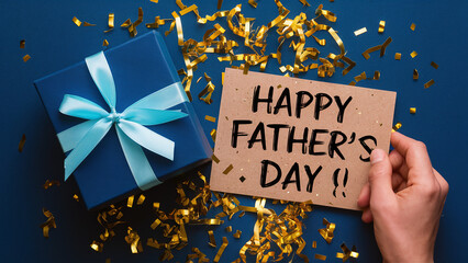 handwritten happy father's day message on greeting card with blue gift box and confetti, flat lay top view - Powered by Adobe
