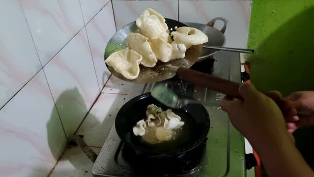 A woman frying shrimp crackers in the kitchen using a black frying pan