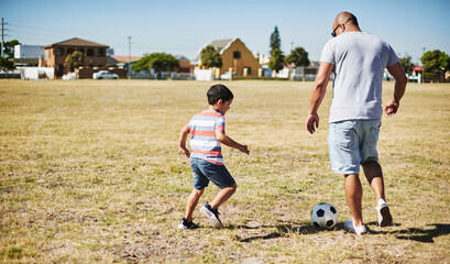 Father, son and playing with soccer ball for sports, fitness in park as family in bonding. Man, boy and fun for activity in together in learning, childhood development or growth on weekend in support