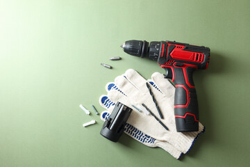 Electric screwdriver, gloves and accessories on pale green background, flat lay