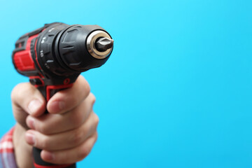 Handyman holding electric screwdriver on light blue background, closeup. Space for text