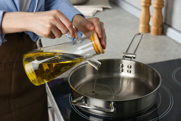 Vegetable fats. Woman pouring cooking oil into frying pan on stove in kitchen, closeup