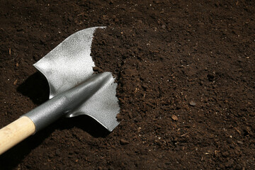 Metal shovel on fertile soil, space for text. Gardening tool