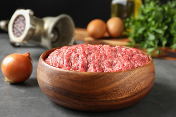 Raw ground meat in bowl and onion on grey table, closeup