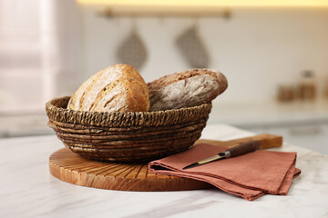 Wicker bread basket with freshly baked loaves on white marble table in kitchen