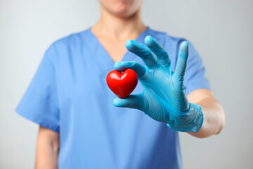 Doctor wearing light blue medical glove holding decorative heart on grey background, closeup