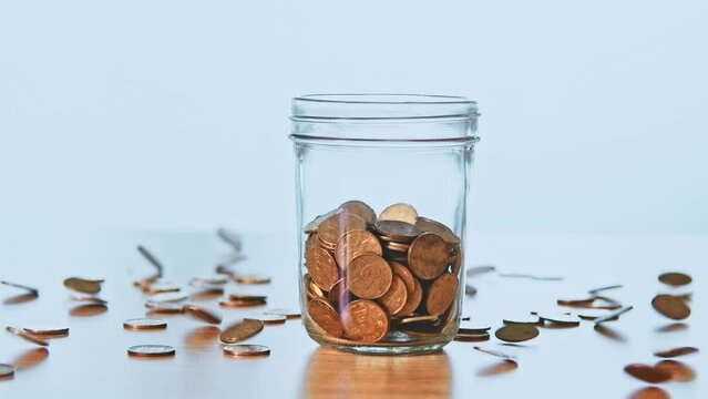 Slow motion video of many coins falling into the jar