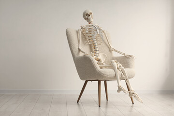 Waiting concept. Human skeleton sitting in armchair indoors, space for text