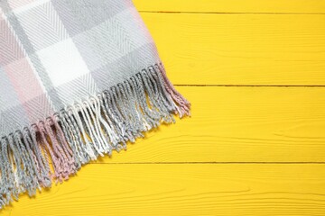 Soft checkered scarf on yellow wooden table, top view. Space for text