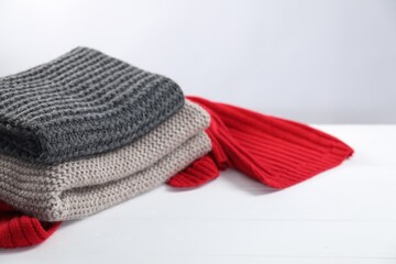 Stylish knitted scarfs on white wooden table, closeup