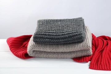 Stylish knitted scarfs on white wooden table