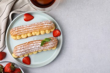 Delicious eclairs filled with cream, strawberries and mint on light table, top view. Space for text
