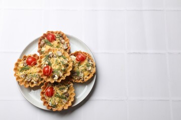 Tasty tartlets with cheese, tomatoes, mushrooms and dill on white tiled table, top view. Space for text