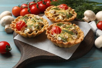 Tasty tartlets with cheese, tomatoes, mushrooms and dill on turquoise wooden table, closeup