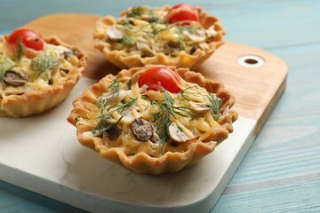 Tasty tartlets with cheese, tomatoes, mushrooms and dill on turquoise wooden table, closeup