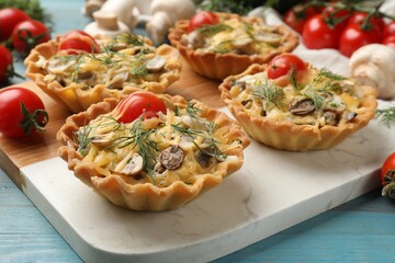 Tasty tartlets with cheese, tomatoes, mushrooms and dill on turquoise wooden table, closeup