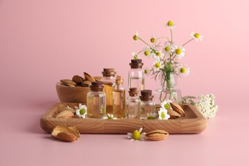 Aromatherapy. Different essential oils, flowers and almonds on pink background
