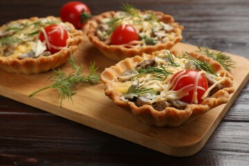 Tasty tartlets with cheese, tomatoes, mushrooms and dill on wooden table, closeup