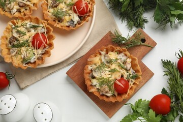 Flat lay composition of tasty tartlets with cheese, tomatoes, mushrooms and dill on white table