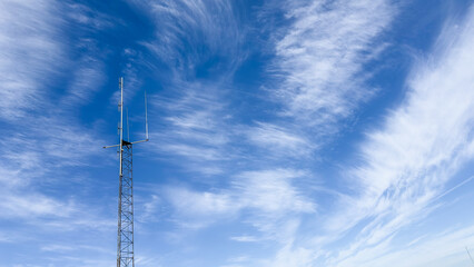 Tall communication tower against clear blue sky with wispy clouds during daytime