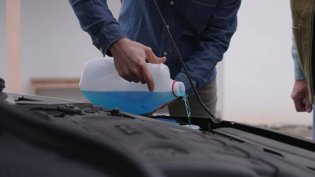 Elderly father teaching son how to refill fluid in a car, coolant in radiator, windshield washer fluid for sprayers. Home car maintenance.
