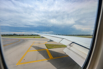 Through the airplane window, Suvarnabhumi International Airport comes into view, along with the expansive wings of the aircraft, amid the midday hustle.