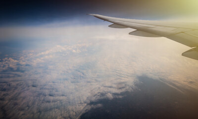 the serene beauty from an airplane window, featuring the wing silhouetted against an expansive, cloud-filled sky, instilling a sense of height and peacefulness.