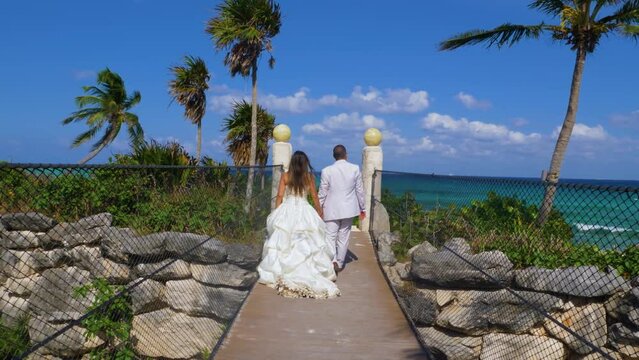unrecognizable newlyweds walking hand in hand on wooden bridge towards the ocean, trash the dress 60fps