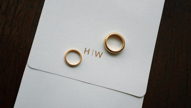 gold wedding rings on invitation with initials H and W written in gold on wooden boards. Jewelry for a married couple. 60fps