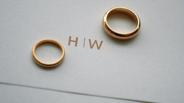 gold wedding rings on invitation with initials H and W written in gold. Jewelry for a married couple. Close up 60fps
