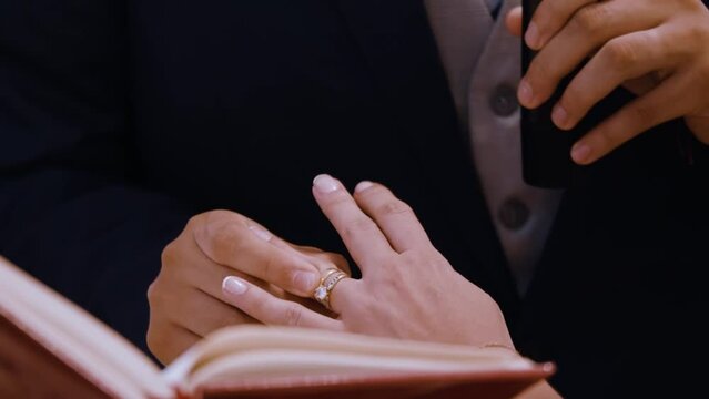 Close up of grooms hand putting a wedding gold ring on the bride's finger. Action 60fps