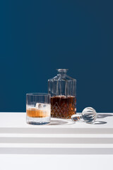 Un vaso de whisky escocés con hielo y decantador sobre fondo azul
