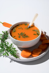 Crema de zanahoria adornada con perejil fresco y guarnición de zanahoria en un plato sobre fondo blanco 	