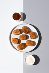 Plato de croquetas fritas con salsa de tomate y mayonesa aperitivo sobre fondo gris y blanco. Vista superior