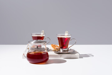 Dos tazas de té rojo con pasteles y dulces sobre mesa blanca y fondo gris