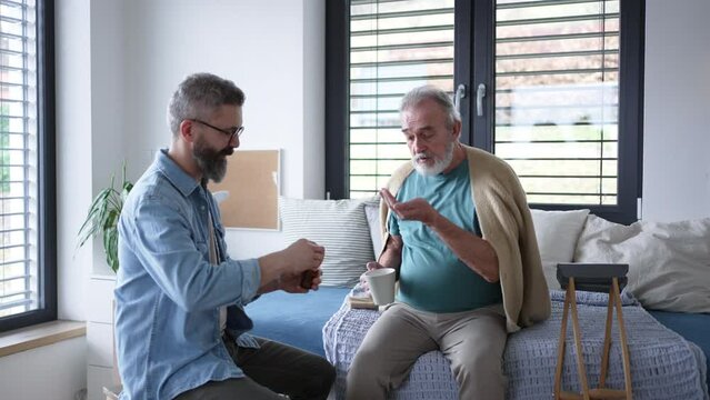 Son giving father prescribed medication. Senior man recovering after surgery, son helping him to return to daily activities. Helping with medication administration.
