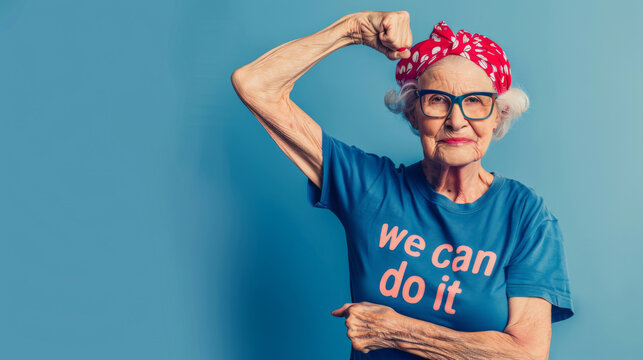 Confident elderly woman in a we can do it shirt flexing arm muscles on blue background