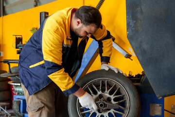 Mechanic adjusting tire on machine, wearing white gloves and blue-yellow uniform. Showcases hands-on automotive repair work and technical skills. Background with yellow walls and garage tools.