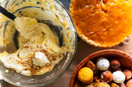half-eaten bannana cream pudding in a large glass serving bowl next to a sweet potato pie and donuts arranged on a table, seen from above